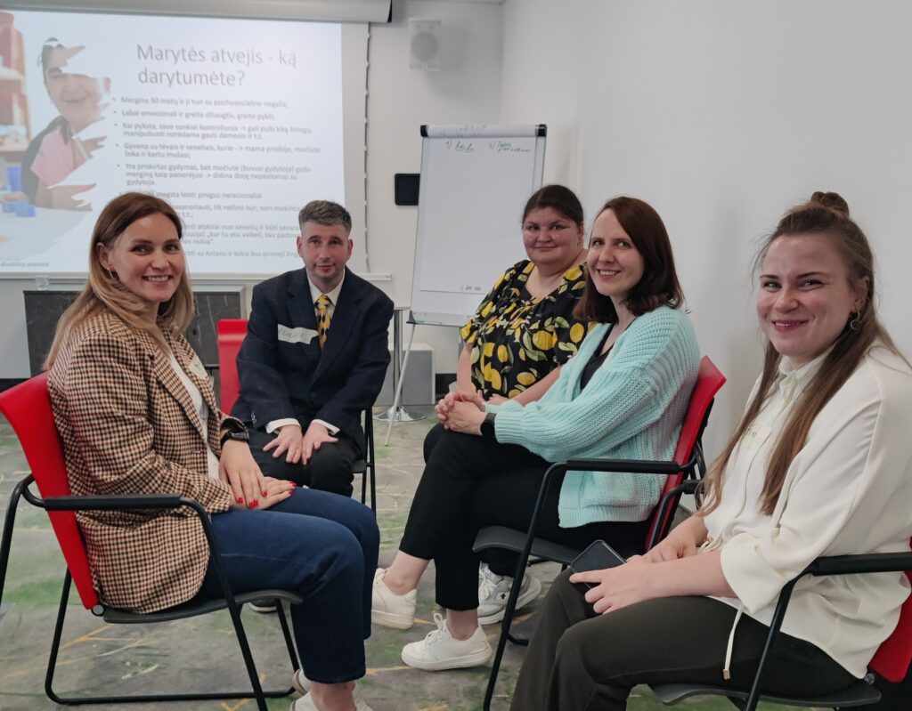 konferencijų salėje ant kėdžių puslankiu sėdi pagalbos priimant sprendimus specialistai, pagalbos priimant sprendimus konsultantė-metodininkė Vitalija Kazragienė ir DUOday iniciatyvos dalyvis Kęstutis. Salės priekyje yra projektorius, kuriame yra skaidrė, joje parašyta „Marytės atvejis – ką darytumėte?“. Prie projektoriaus yra lenta su dideliais popieriais, skirtais ant jų rašyti.