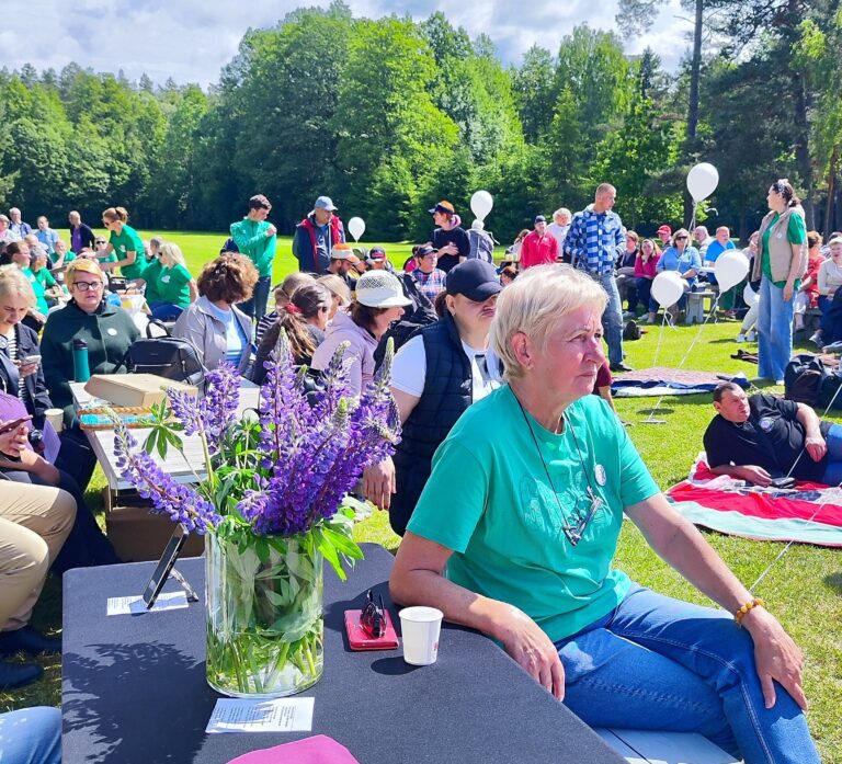 Lauke, vasaros metu, vyksta šventė, ant žolės yra daug stalų, prie jų sėdi žmonės. Kiti žmonės sėdi ant žolės, pasitiesę paklodes. Priekyje prie stalo sėdi Tinklaveikos specialistė Marijona Janavičienė