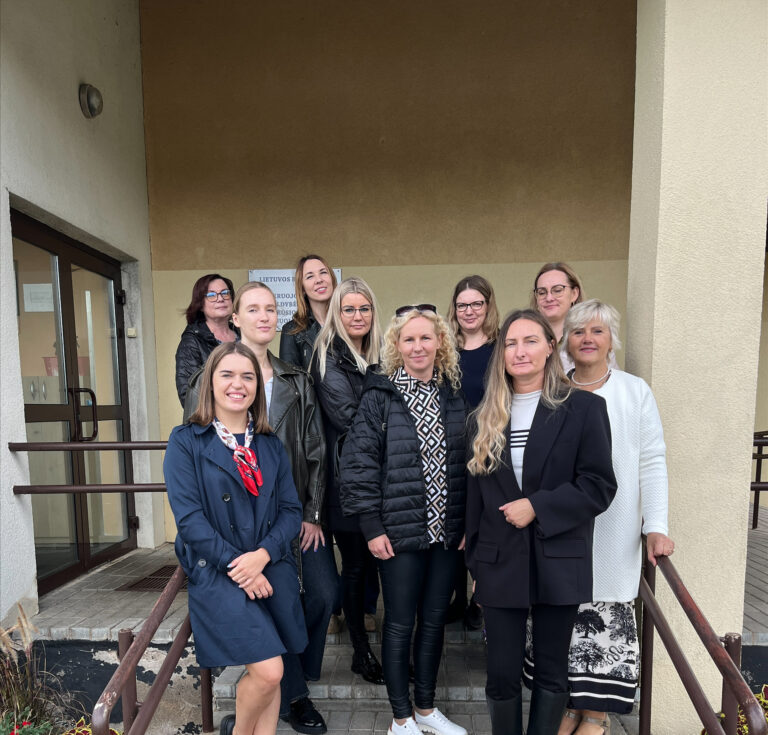 Apie 10 moterų (atvejo vadybininkių, savivaldybės darbuotojų) stovi ant pastato laiptų, pozuoja nuotraukai, šypsosi.