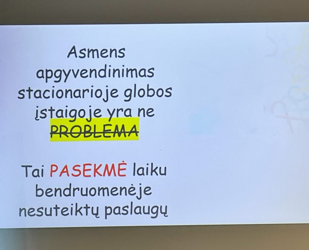 Nuotraukoje skadrė, kurioje parašyta: asmens apgyvendinimas stacionarioje globos įstaigoje yra ne PROBLEMA (žodis PROBLEMA pageltonintas ir nubrauktas). Tai PASEKMĖ (žodis PASĖKMĖ parašytas raudona spalva) laiku bendruomenėje nesuteiktų paslaugų.