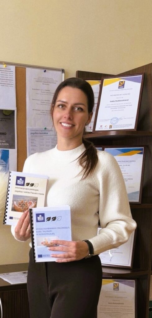 Nuotraukoje matoma moteris, stovinti biuro patalpoje. Ji atsisukusi į kamerą, šypsosi, atrodo rami ir draugiška. Moteris vilki šviesų, ilgomis rankovėmis megztinį, jos tamsūs plaukai surišti atgal.
Rankose ji laiko dvi nedideles lengvai suprantamos kalbos metodines knygeles su spalvotais viršeliais – viena mėlyna, kita gelsva. Ant viršelių matyti iliustracijos ir tekstas.
Už moters nugaros – lentyna su įrėmintais dokumentais, diplomais ir sertifikatais. Taip pat matosi skelbimų lenta su prisegtais lapais. 
