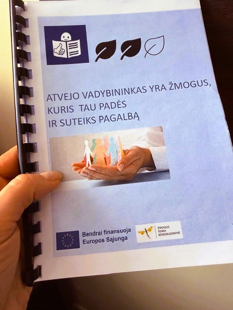 Nuotraukoje matomas lengvai suprantamos kalbos metodines knygeles viršelis, laikomas žmogaus rankoje. Kairėje pusėje aiškiai juntamas spiralinis įrišimas – plastikinė spiralė, einanti per visą kraštą. Fonas šviesiai melsvas.
Viršutinėje viršelio dalyje yra keli paprasti simboliai: piktograma su žmogeliuku, skaitančiu knygą, ir trys lapų formos ikonėlės. Žemiau – didelis, lengvai įskaitomas tekstas lietuvių kalba:
„Atvejo vadybininkas yra žmogus, kuris tau padės ir suteiks pagalbą.“
Po tekstu matoma iliustracija: delnuose laikomos mažos, stilizuotos žmonių figūrėlės. Rankos atrodo kaip saugantis, globojantis gestas, o figūrėlės simbolizuoja skirtingus žmones ar bendruomenę.
Apatinėje viršelio dalyje yra logotipai. Vienas jų – Europos Sąjungos vėliava su užrašu „Bendrai finansuoja Europos Sąjunga“. Šalia – Pertvarkos projekto logotipas.
